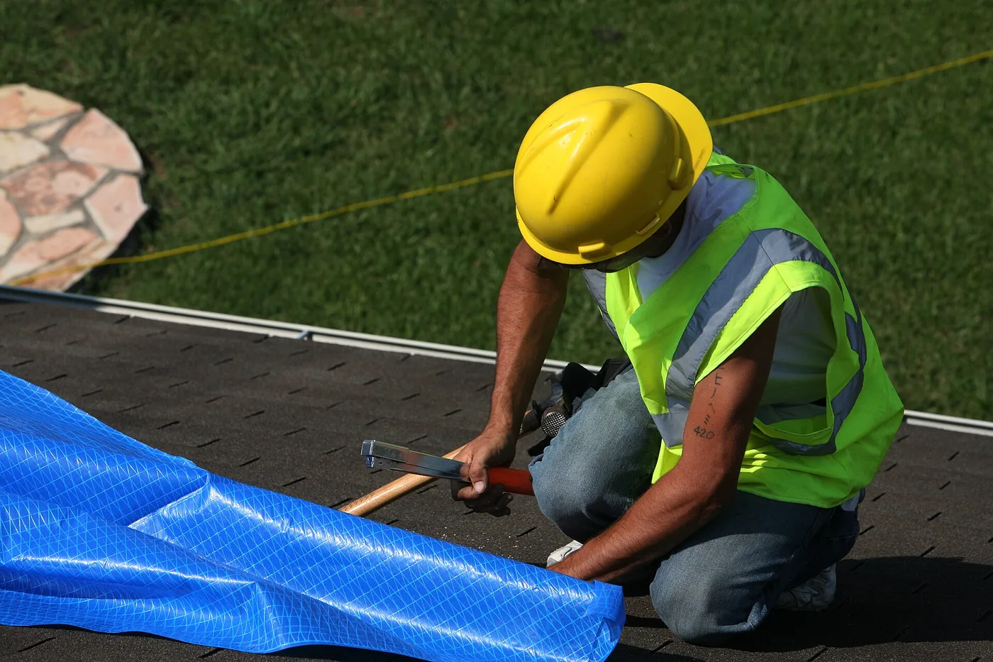 Roofer fastening a blue emergency roof tarp on a storm-damaged shingle roof – emergency roof tarping Pensacola